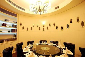 Une table de salle à manger ronde, entourée de chaises en cuir noir, un lustre et un mur orné de miroirs ovales.