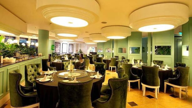 Un comedor amplio con mesas redondas y sillas tapizadas en verde, con un diseño de techo moderno que incluye iluminación empotrada.