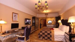Una habitación de hotel con cama, escritorio, silla, televisor y candelabro.