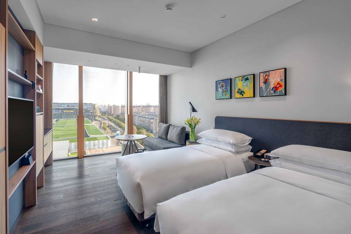 Une chambre d’hôtel moderne avec deux lits, une télévision, une petite table et une vue sur la ville.