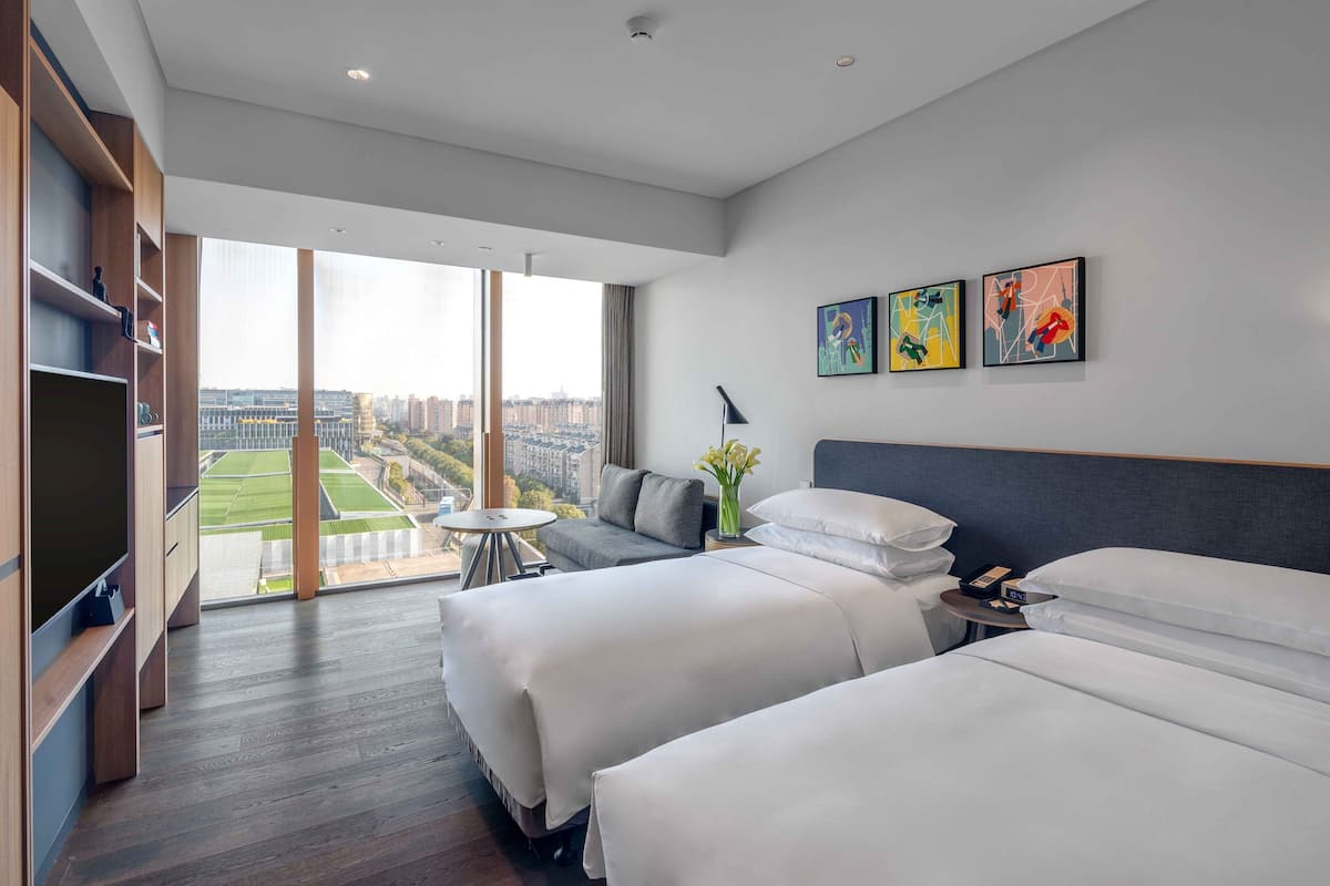 Une chambre d’hôtel avec deux lits, une télévision, une petite table et des œuvres d’art accrochées au mur.
