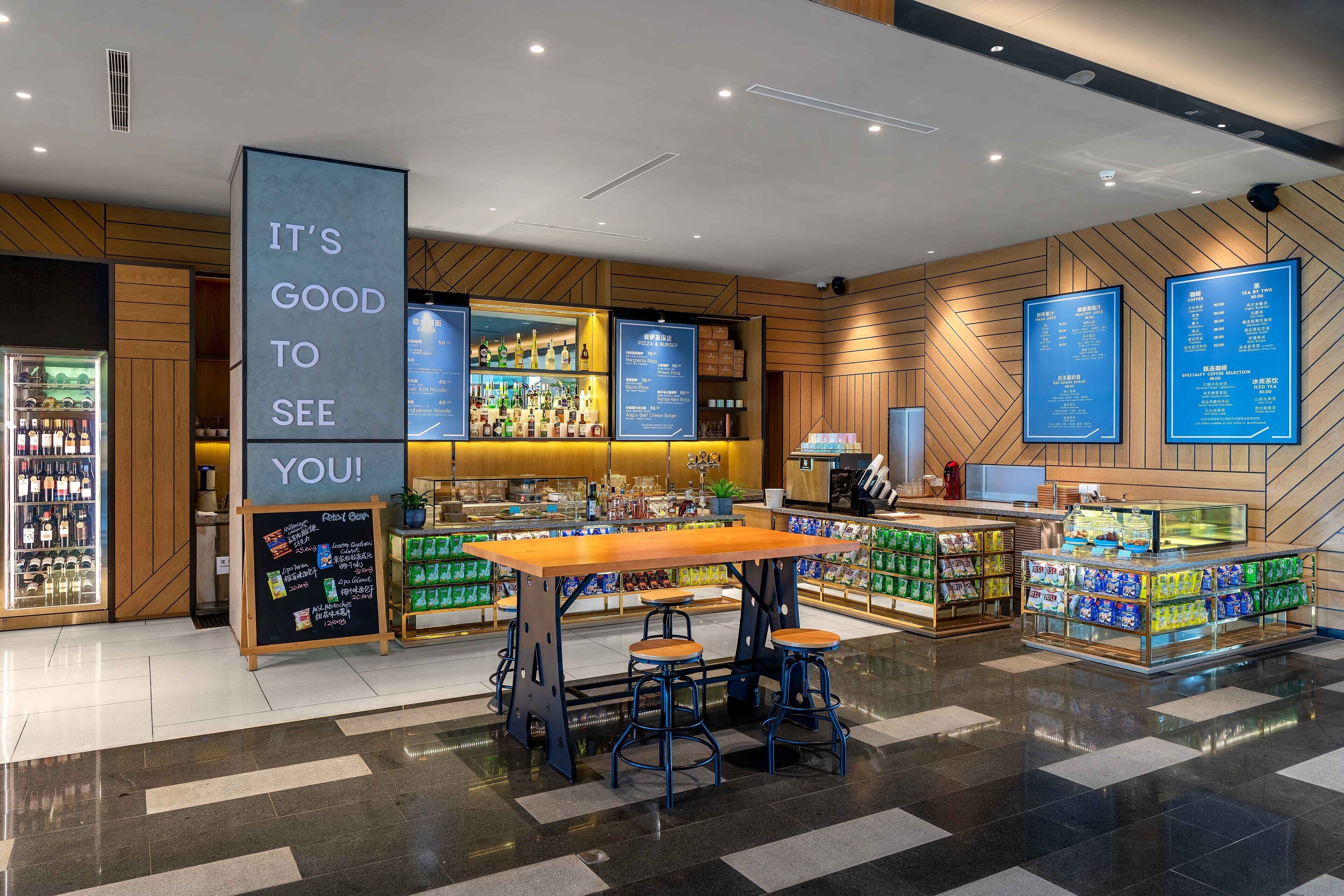 A modern retail area with a central wooden table and bar stools, surrounded by shelves stocked with various products.