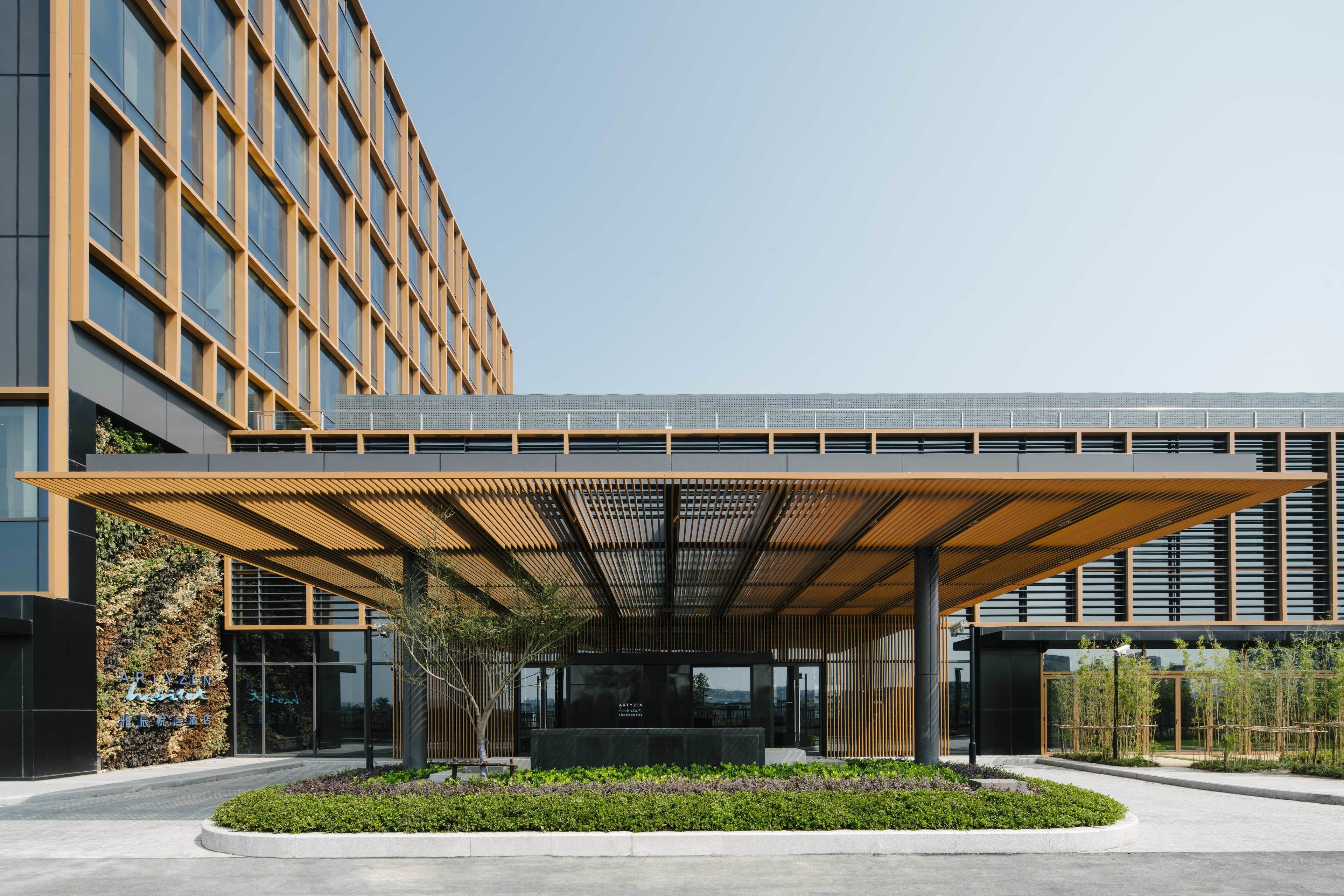 A modern building with a covered entrance, a landscaped garden, and a sign indicating it is a hotel.