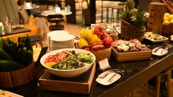Un bufé con diversos platos, incluyendo ensaladas, frutas y carnes.