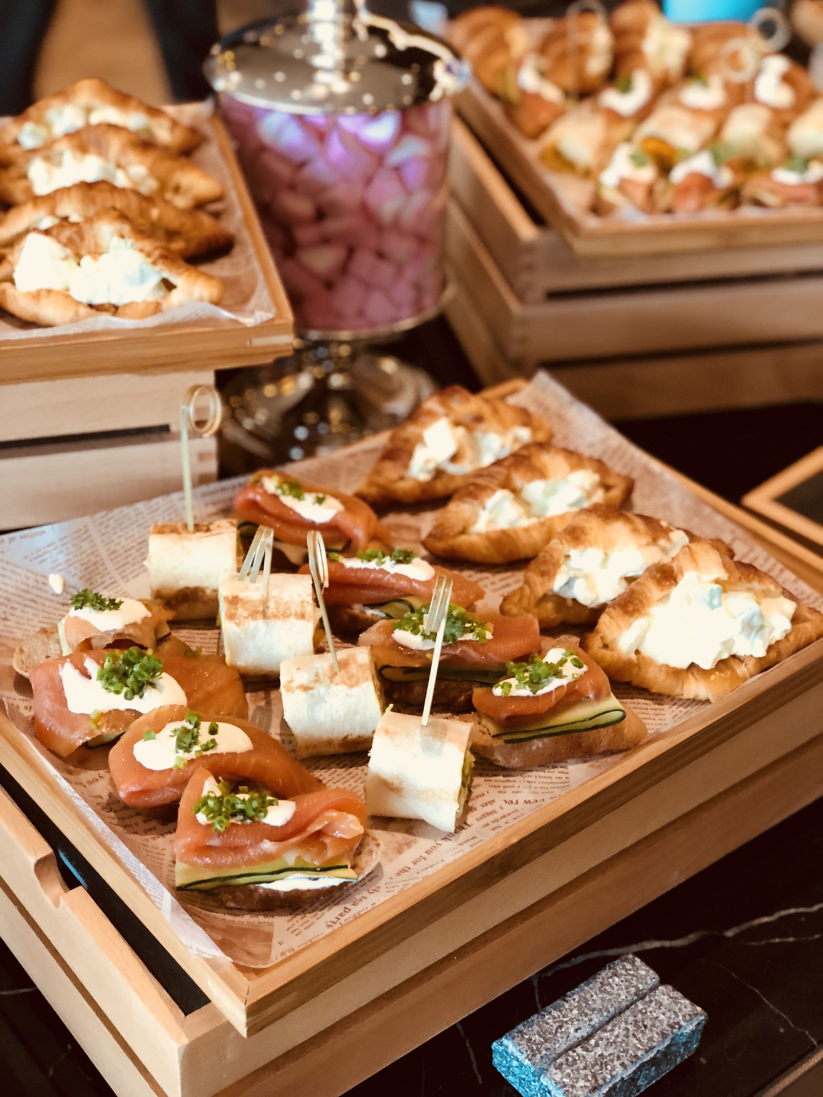 A tray of appetizers including smoked salmon and cream cheese on bread, arranged on a wooden board.