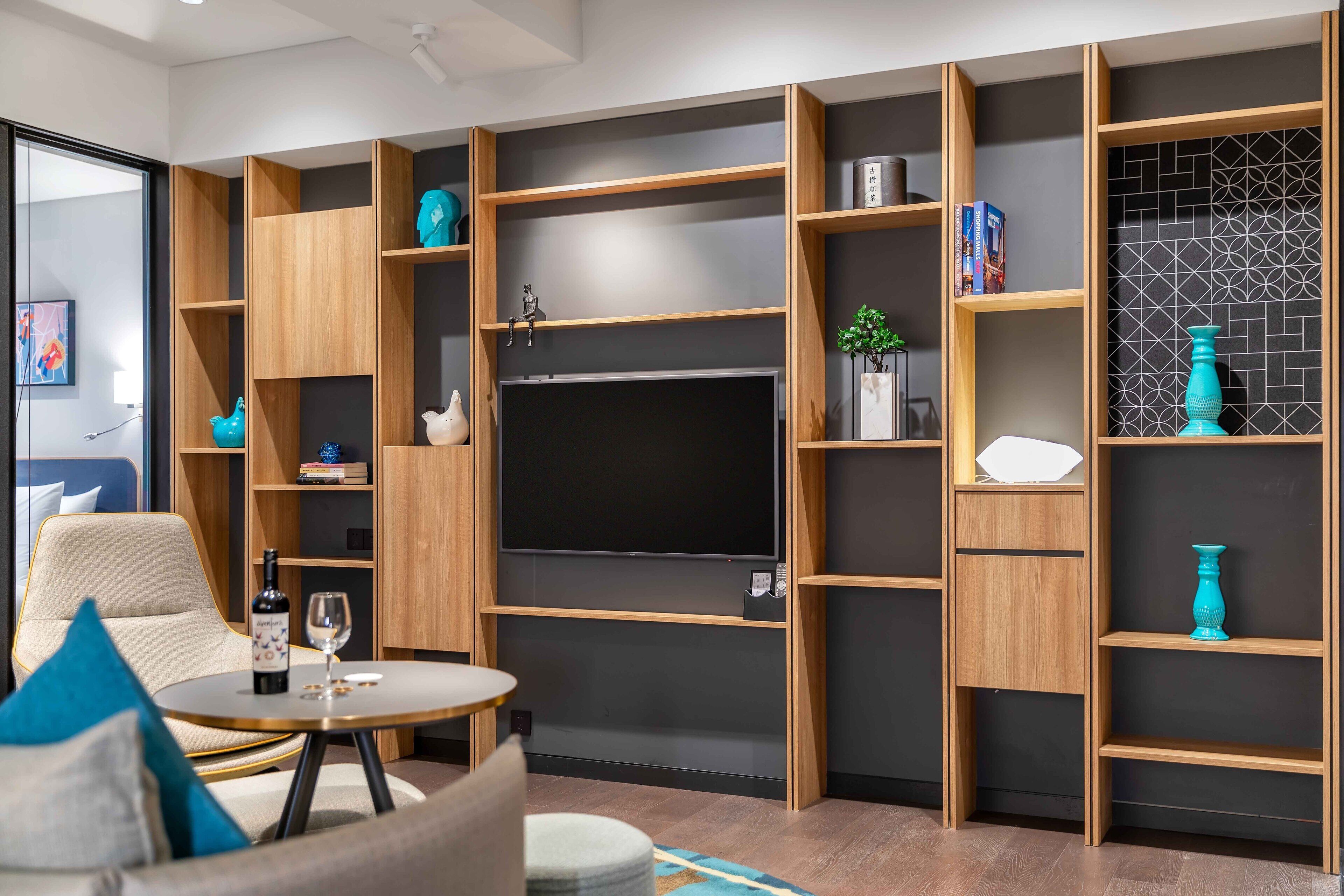 A modern living room with a flat-screen TV, wooden shelving, a sofa, and a small round table with a bottle and glass.
