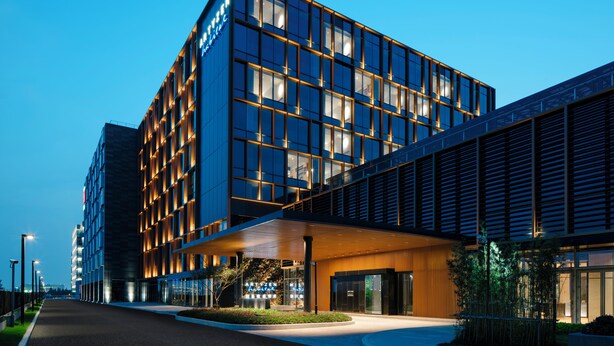 Ein modernes Hotel mit Glasfassade, überdachter Eingangspartei und einer begrünten Fläche davor.