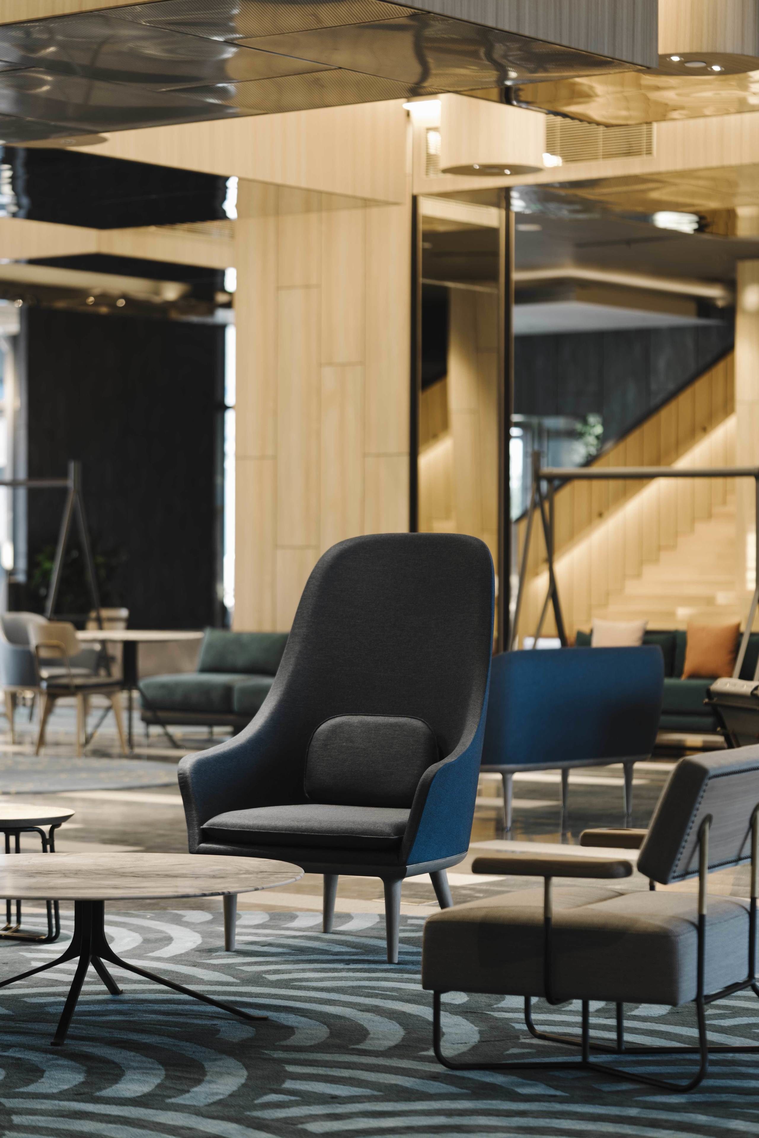 Eine moderne Lobby mit einem großen grauen Sessel, einem blauen Sofa und einem gemusterten Teppich.