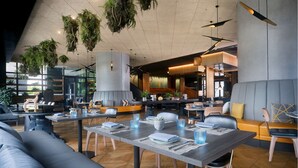 Ein modernes Restaurant mit hohen Decken, hängenden Pflanzen und einer Mischung aus Sitzgelegenheiten, darunter Tische und Sofas.