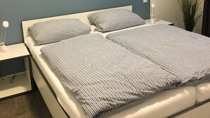 Moderni makuuhuone, jossa on sänky, yöpöydät ja ruukkukasvi.