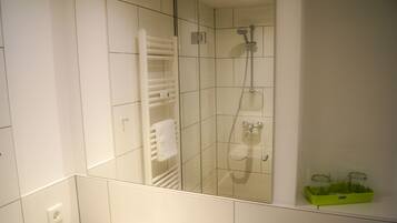 A modern bathroom with white tiles, a glass-enclosed shower, a white towel rack, and a green soap dish.