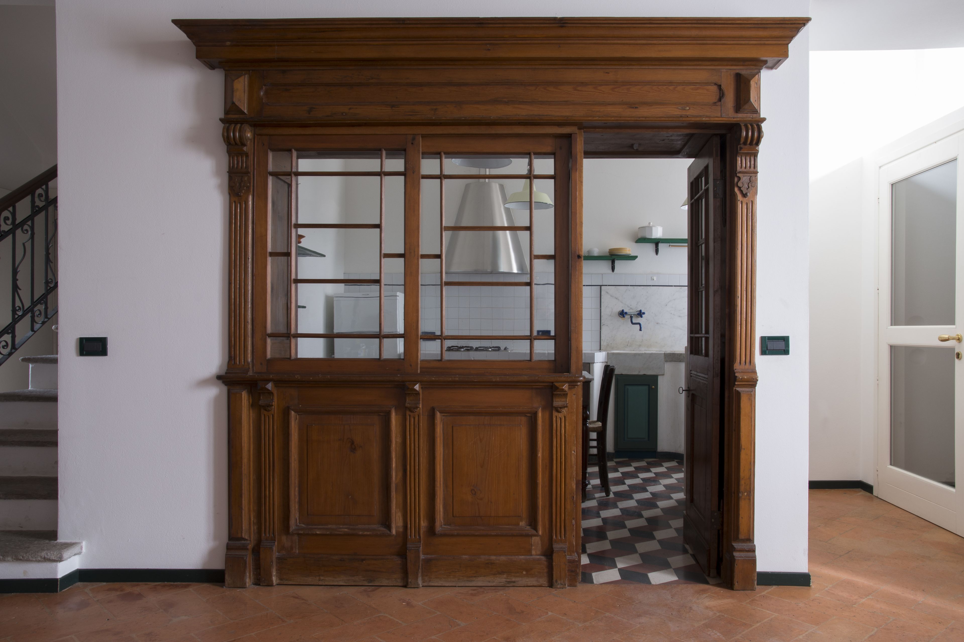 Eine Holztür mit Glasfeldern, ein Schachbrettfußboden und eine Treppe links.