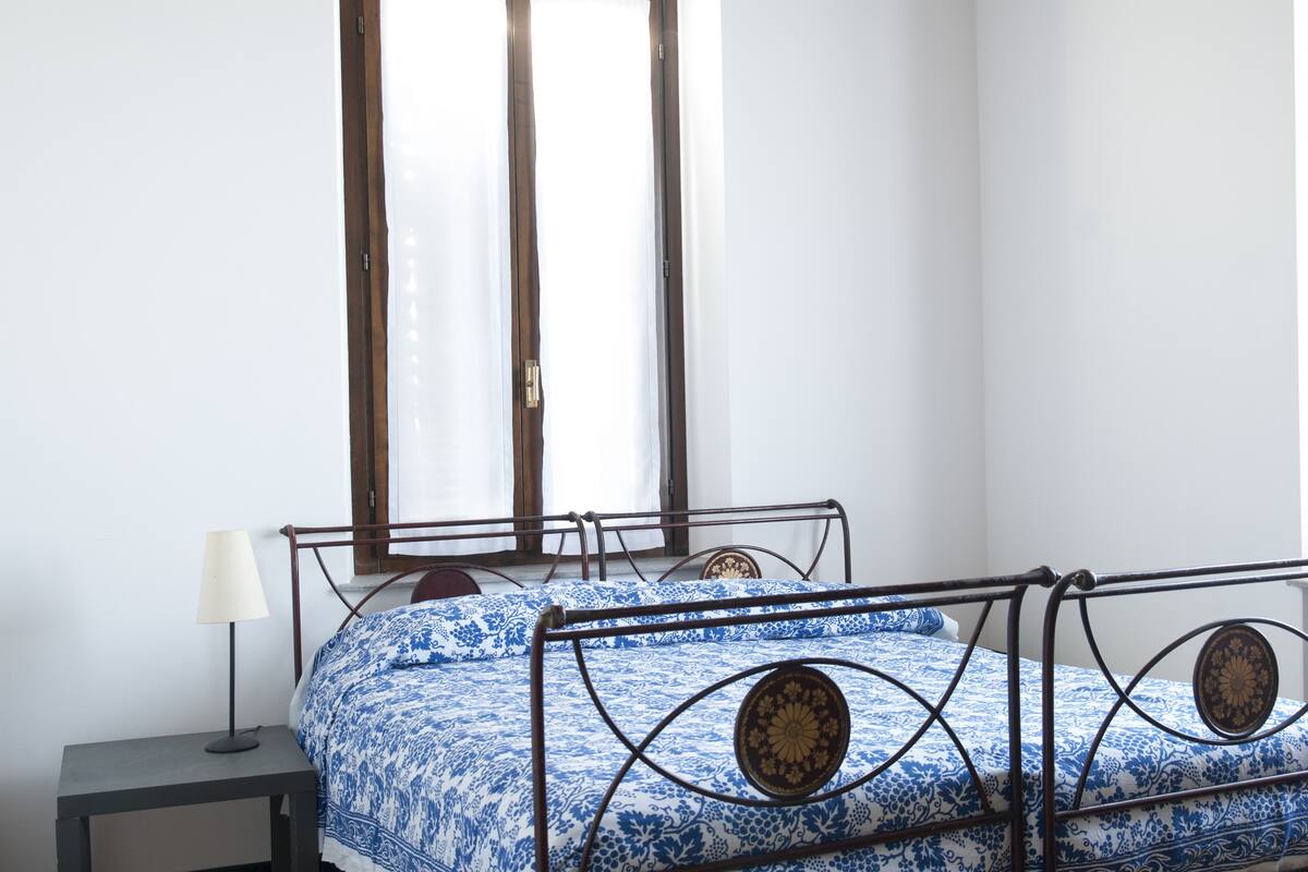 Une chambre à coucher avec un lit en métal, une table de chevet avec une lampe et une fenêtre avec des rideaux.