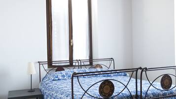 A bedroom with a metal bed frame, a bedside table with a lamp, and a window with curtains.