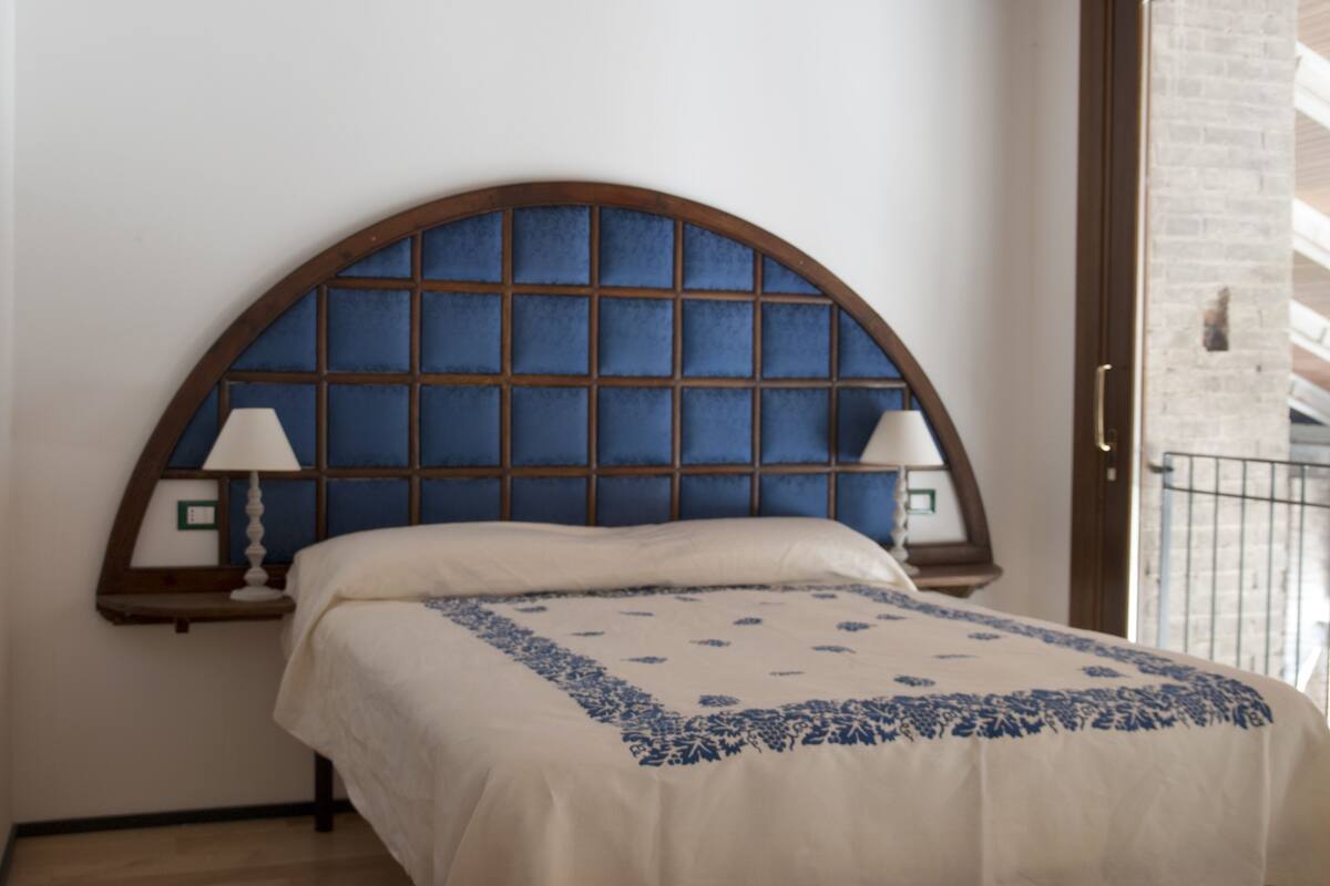 Une chambre à coucher avec un lit, deux lampes de chevet et une fenêtre ornée d’un motif à carreaux bleus.