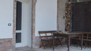 An interior space with a brick wall, a white door, a wooden bench, and a large dark wooden cabinet. - Palazzo Turro B&B (Podenzano)