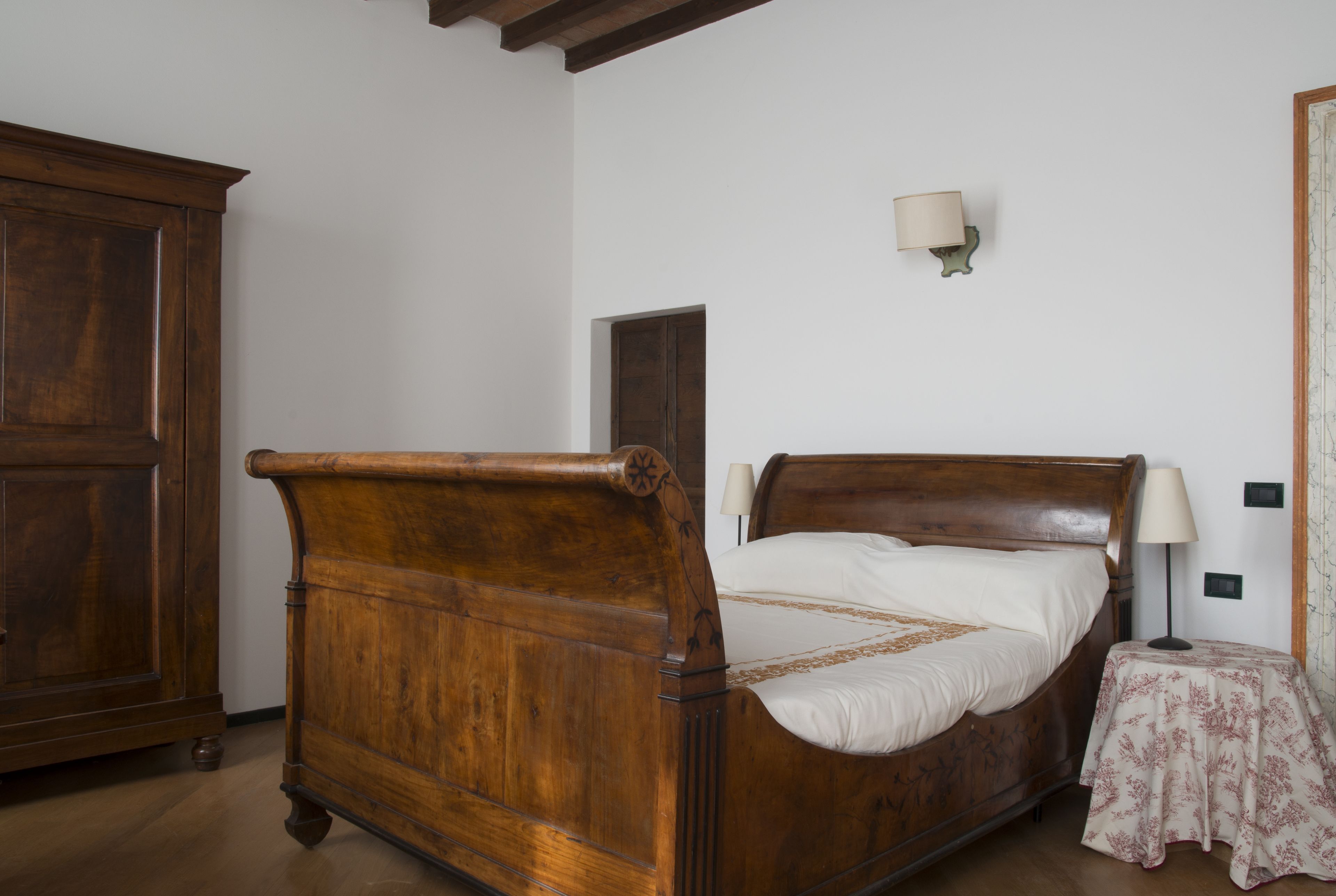 A bedroom with a wooden bed, a nightstand with a lamp, and a wardrobe.