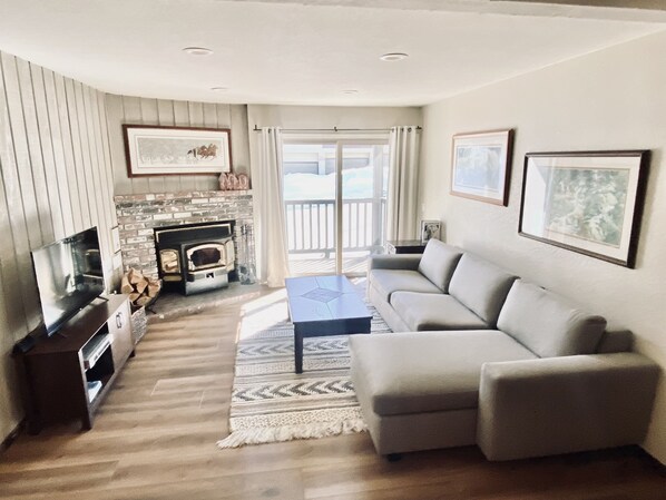 A living room with a fireplace, a sofa, a TV, and a large window.