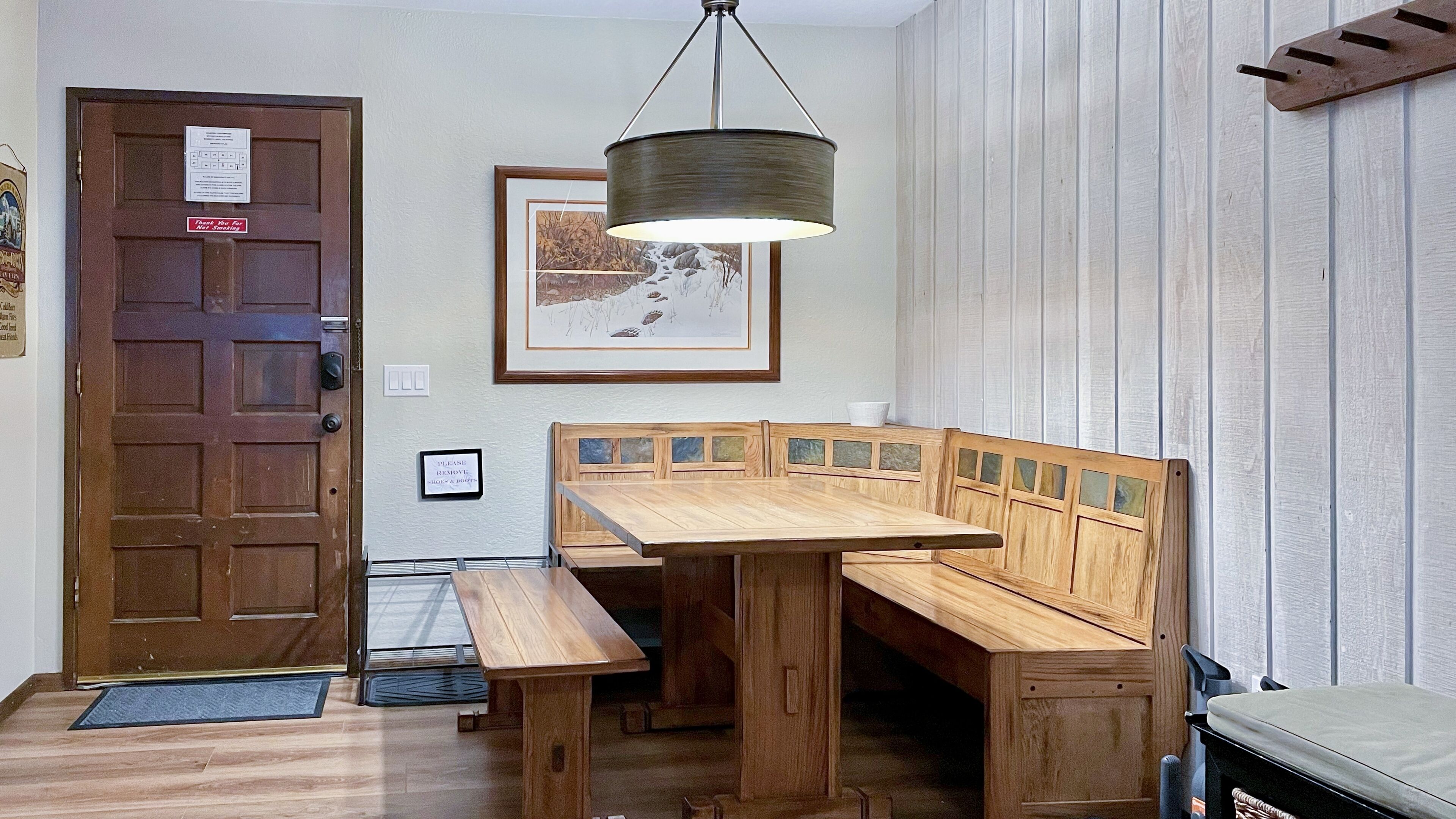A wooden dining table with benches, a hanging light fixture, a door with a sign, and a framed picture on the wall.