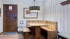 A wooden dining table with benches, a hanging light fixture, a door with a sign, and a framed picture on the wall.