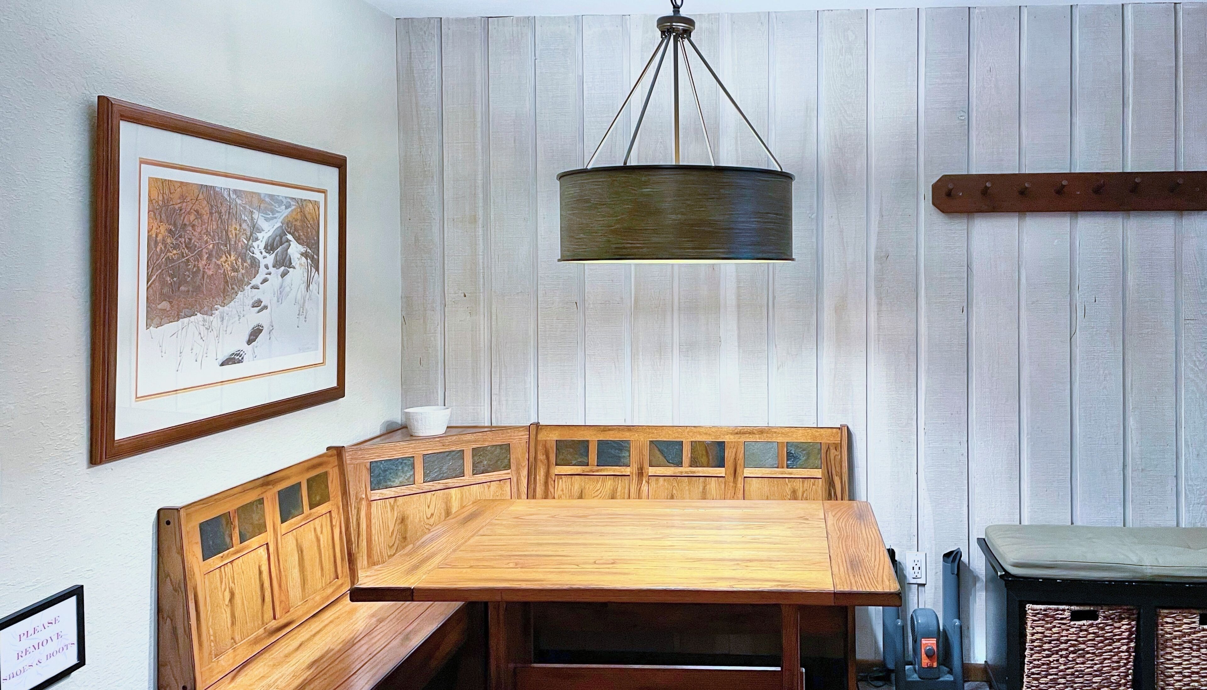 A wooden bench with a cushioned seat and backrest, a framed picture on the wall, and a hanging light fixture.