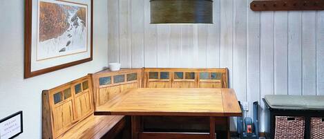 A wooden bench with a cushioned seat and backrest, a framed picture on the wall, and a hanging light fixture.