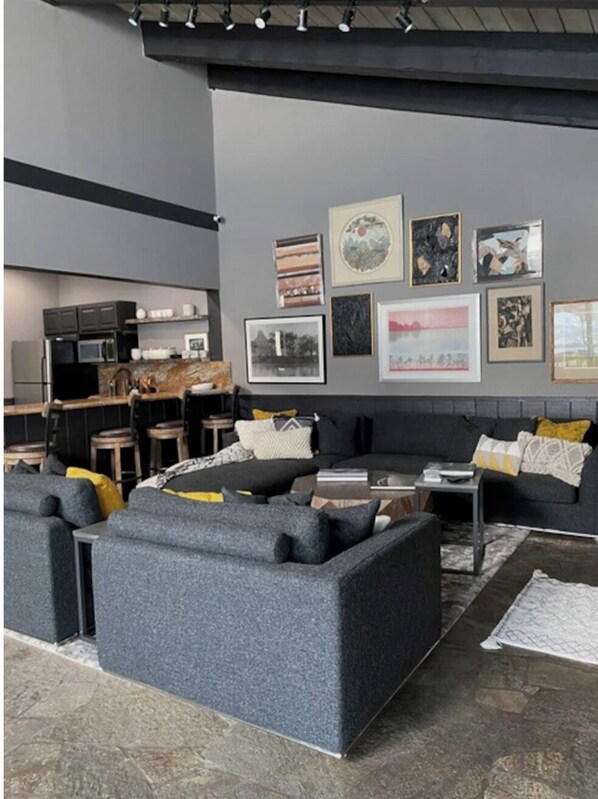 A modern living room with grey sofas, a coffee table, and a kitchen area in the background.