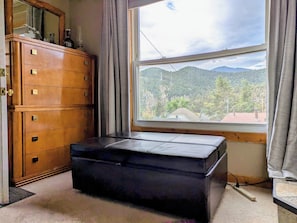 A room with a wooden dresser, a black ottoman, and a window with a view of mountains. - Cozy Idaho Springs Cabin: near Historic District, Hot Springs, Rafting & Trails (Idaho Springs)