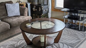 Un salon chaleureux avec une table basse ronde en bois, un canapé, une malle ancienne, un téléviseur et une lampe.