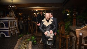 A man in a leather coat holding a small dog inside a rustic interior with wooden furniture and a decorative pool. - Egorkino Hotel (Astana)