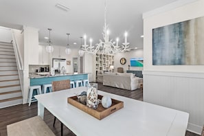 A modern kitchen with white cabinets, a blue countertop, and a central island. There is a dining area with a white table and a decorative tray.