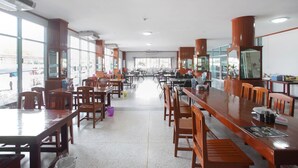 Een ruim restaurant met lange houten tafels en stoelen, grote ramen en een lichte inrichting.