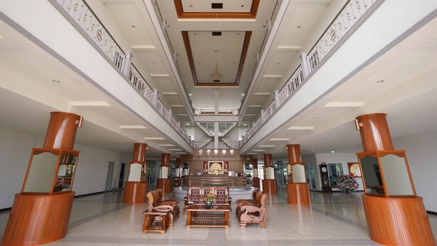 Een ruime lobby met een hoge plafond, een centraal gelegen receptiebalie en een zithoek met houten meubels.