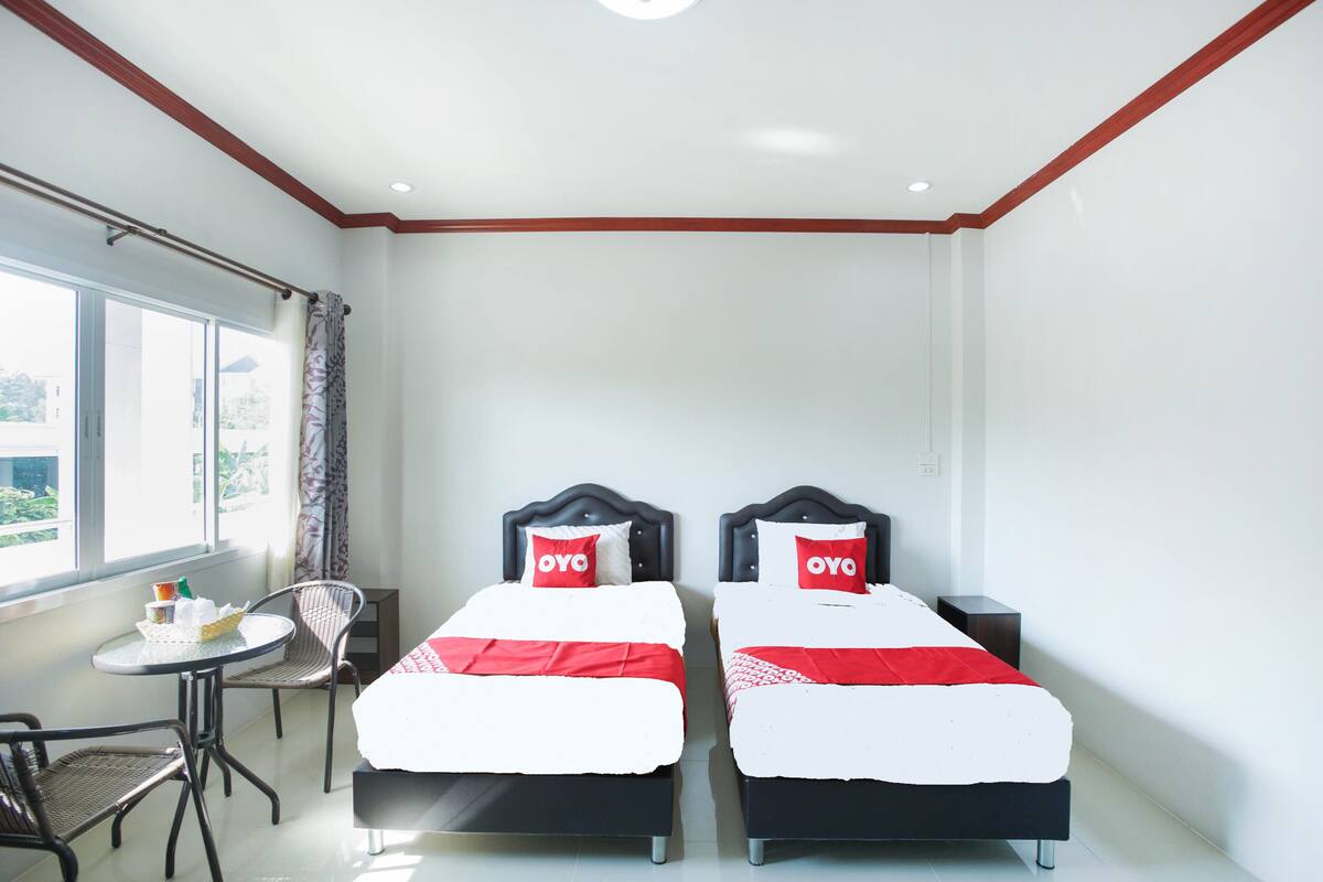 Een hotelkamer met twee bedden, een klein tafeltje met stoelen en een raam met uitzicht op groen.
