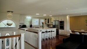 A modern kitchen with white cabinetry, a central island with bar stools, and a dining area with a wooden table and chairs. - Scenic Lake View Home (Tacoma)