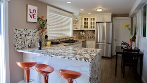A modern kitchen with a marble countertop, stainless steel appliances, and three orange bar stools. - Scenic Lake View Home (Tacoma)