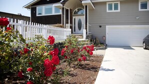 A two-story house with a white picket fence, a garage, and a garden with red roses. - Scenic Lake View Home (Tacoma)