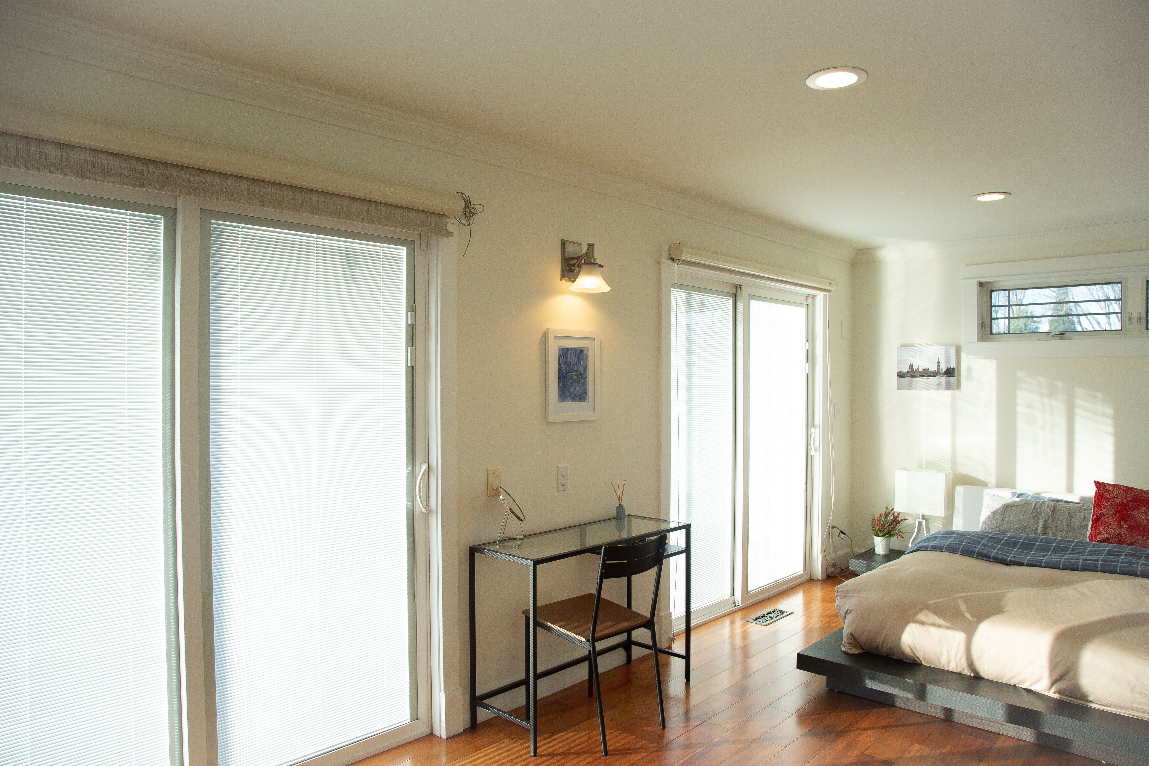 A bedroom with a bed, a desk, and a chair. There are sliding glass doors and a window.