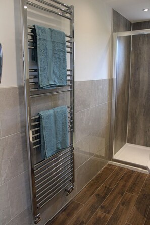 Une salle de bain avec une douche à parois de verre, un porte-serviettes avec deux serviettes et un plancher en bois.