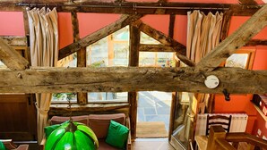 A rustic interior with exposed wooden beams, a red wall, and a green hanging light fixture. - Llethrau Farm (Knighton)
