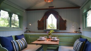 A dining area with green upholstered benches, a wooden table set for two, and a decorative window above. - Llethrau Farm (Knighton)