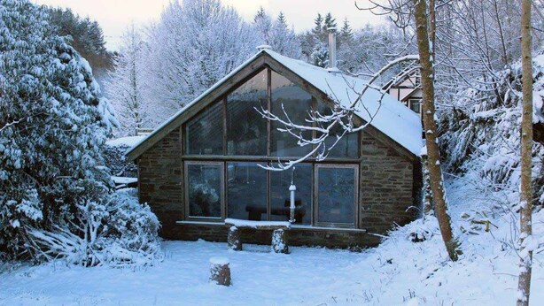 A wooden cabin with large windows, surrounded by snow-covered trees and a snowy landscape. - Llethrau Farm (Knighton)