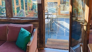 A cozy room with a wooden ceiling, a glass door leading outside, and a cushioned bench with a green pillow. - Llethrau Farm (Knighton)