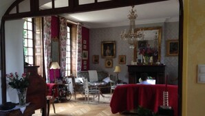 Una habitación tradicional con suelo de madera, un sofá rojo, una mesa con mantel rojo y una araña.