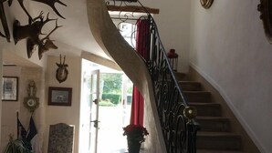 Una imponente escalera con alfombra roja que conduce a una puerta, rodeada de diversas decoraciones en las paredes, incluyendo cabezas de animales y cuadros enmarcados.
