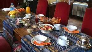 Una mesa de comedor dispuesta para el desayuno, rodeada de sillas rojas, en una habitación con vistas a la vegetación por la ventana.