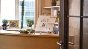 A reception area with a wooden counter, a welcome sign, and a door. - Mettner Hof (Metten)