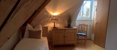 Ein gemütliches Schlafzimmer im Dachgeschoss mit schrägen Wänden, einem Bett, einem Nachttisch, einer Lampe, einem Sessel und einem Schrank.
