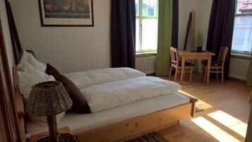 Een slaapkamer met een houten bed, een tafel met stoelen, een lamp en een raam met gordijnen.