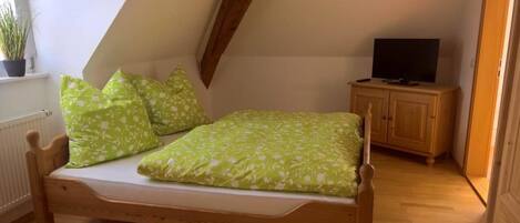 Una habitación pequeña y acogedora con una cama de madera, un televisor sobre un mueble de madera y una ventana con una planta.